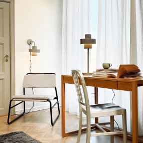 Stoke Ø15 Varm grå vegglampe Fra Dyberg Larsen - Den er laget av metall med en blank overflate som fremhever de sylindriske formene på lampen og skaper en balansert kontrast med andre materialer som stein, tre.