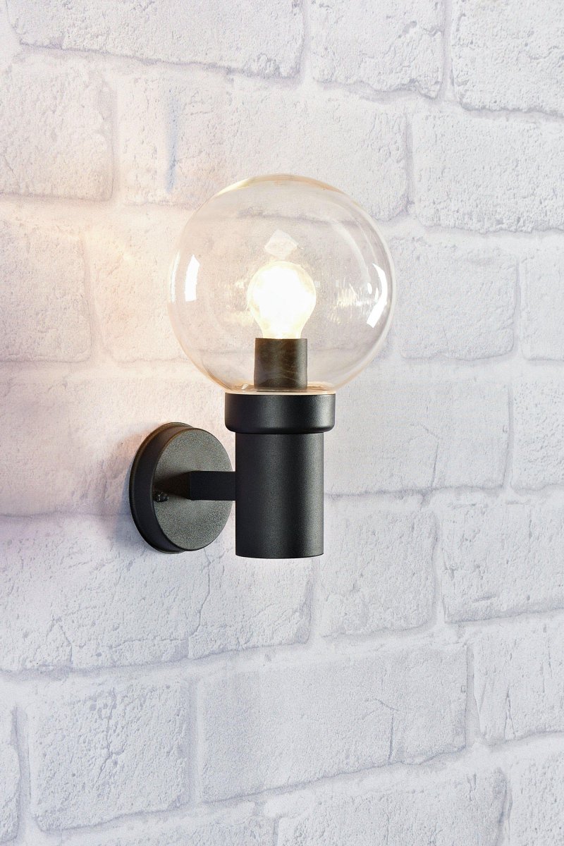 Caris Svart utendørslampe Fra Markslöjd - Med en robust, sort metallfot og en stor, klar glasskuppel sprer lampen et klart og behagelig lys som skaper en innbydende atmosf&aelig;re.