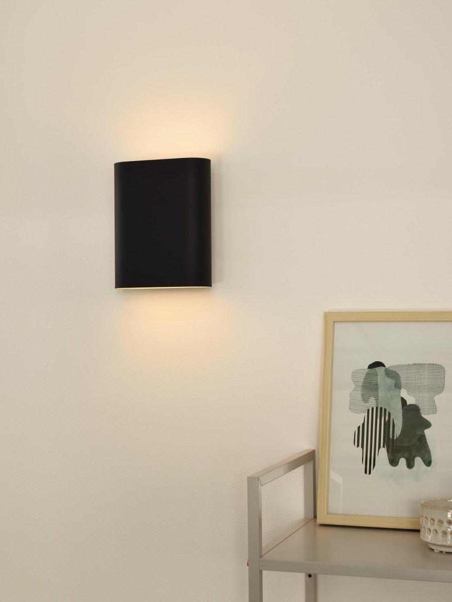 Ovalis 20cm Svart vegglampe Fra Lucide - Ovalis skaper en vakker timeglassformet lyseffekt på veggen, og med sitt gylne interiør skaper den en varm atmosfære i rommet.