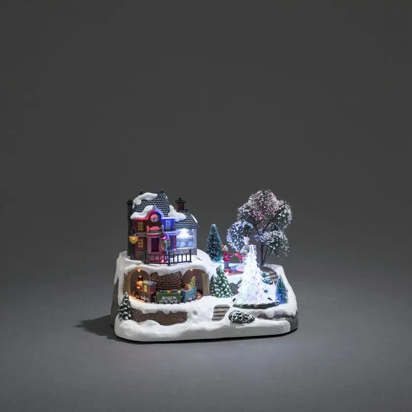 Mekanisk Juledekorasjon Med Togstasjon 17cm Flerfarget Fra Konstsmide - G&aring; inn i en vinterlig miniatyrverden med denne mekaniske juledekorasjonen &ndash; en sjarmerende togstasjon i rolige omgivelser.