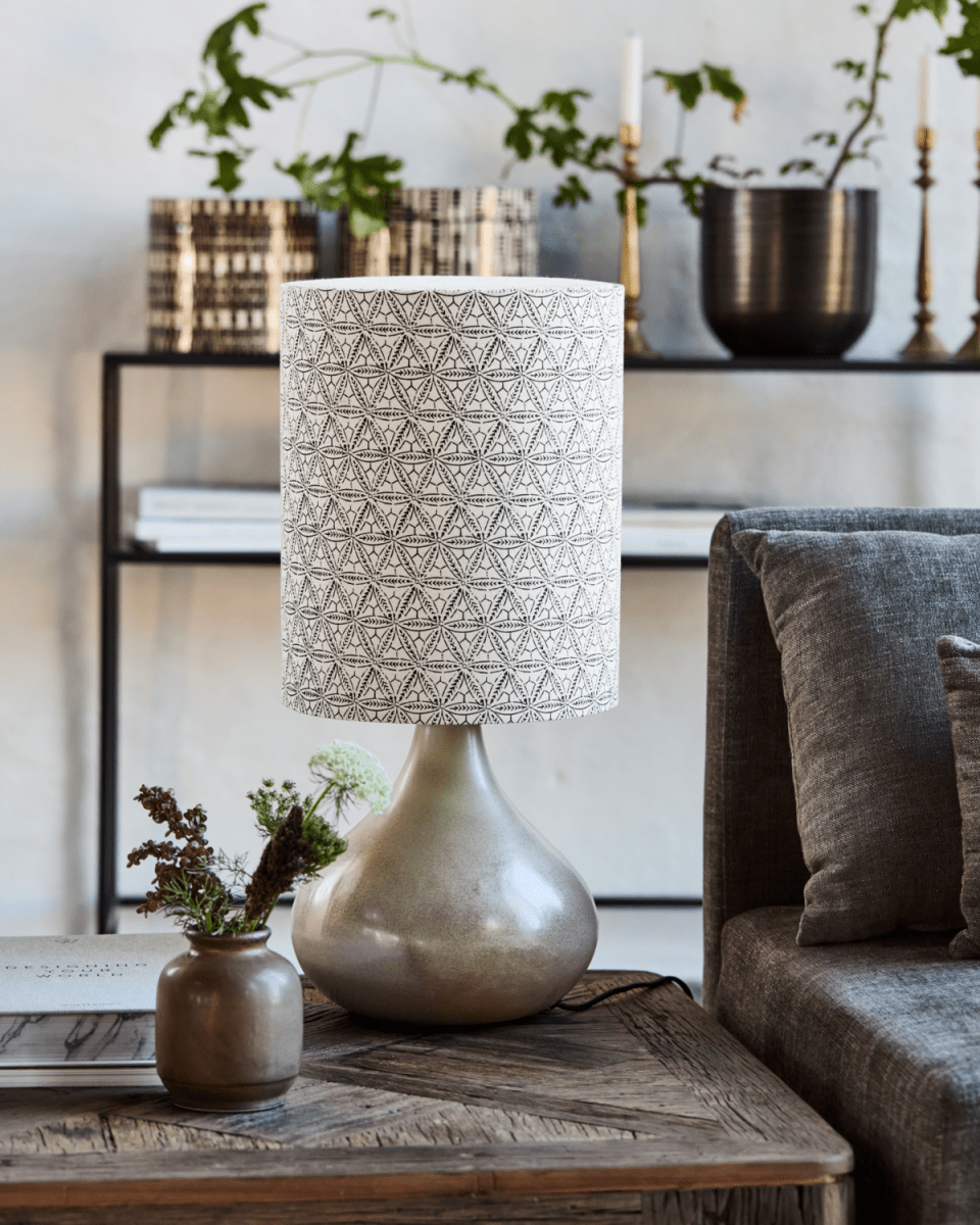 Florie 60cm Sand bordlampe Fra House Doctor - Den keramiske basen i en beroligende sandskygge gir et stabilt og elegant fundament, mens lampeskjermen i lin viser et håndtrykt svart etnisk mønster for en unik og kunstnerisk følelse.