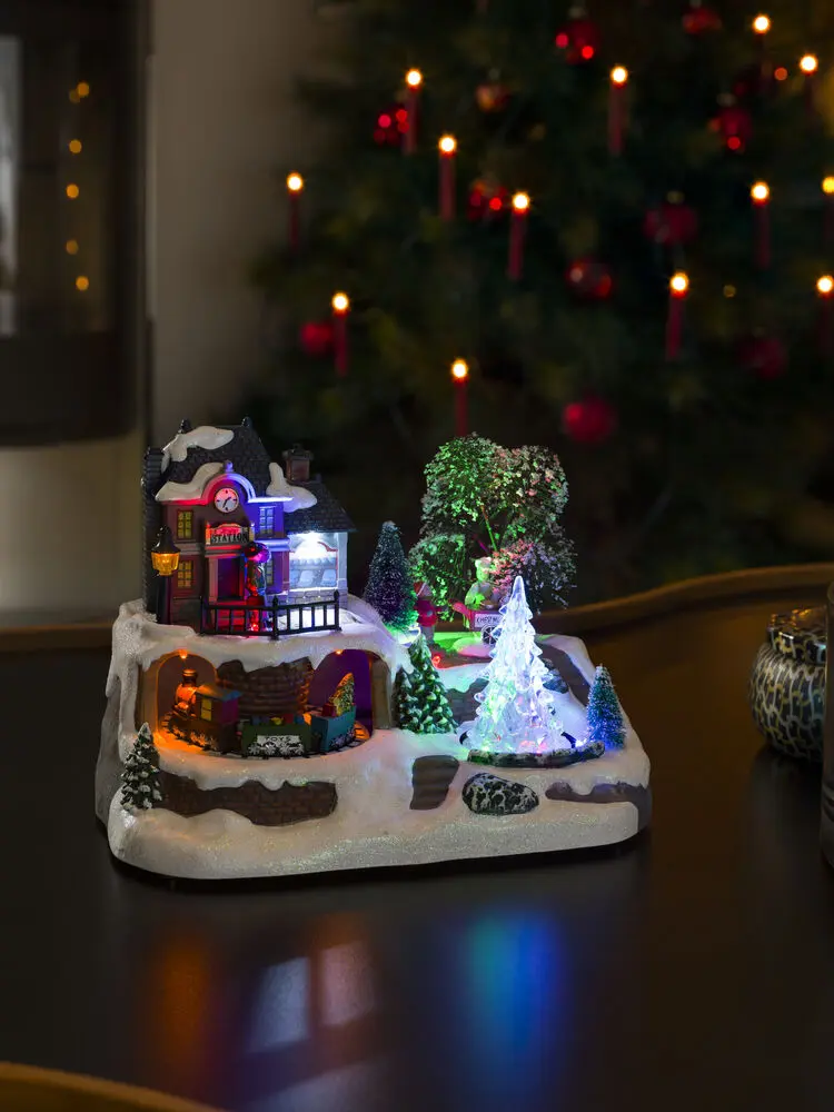 Mekanisk Juledekorasjon Med Togstasjon 17cm Flerfarget Fra Konstsmide - G&aring; inn i en vinterlig miniatyrverden med denne mekaniske juledekorasjonen &ndash; en sjarmerende togstasjon i rolige omgivelser.