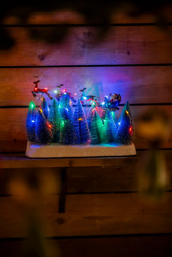 Nisse Med Slede 22cm Flerfarget Fra Konstsmide - Juledekorasjon med julenissen i sn&oslash;drakt som flyr over sn&oslash;dekte grantr&aelig;r.
