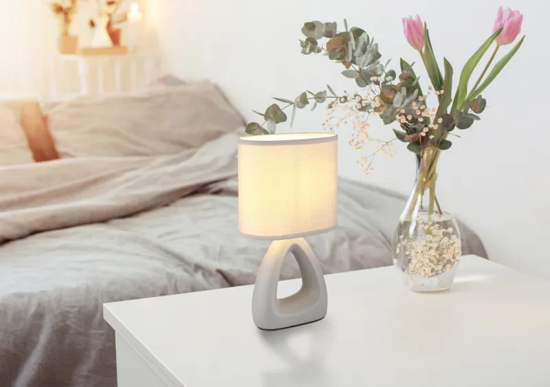 Triangle 30cm Grå bordlampe Fra Globo Lighting - Den triangelformade basen med ett stilrent utskuret h&aring;l ger ett modernt intryck, medan den ovala textilsk&auml;rmen i gr&aring; f&auml;rg sprider ett behagligt och j&auml;mnt ljus.