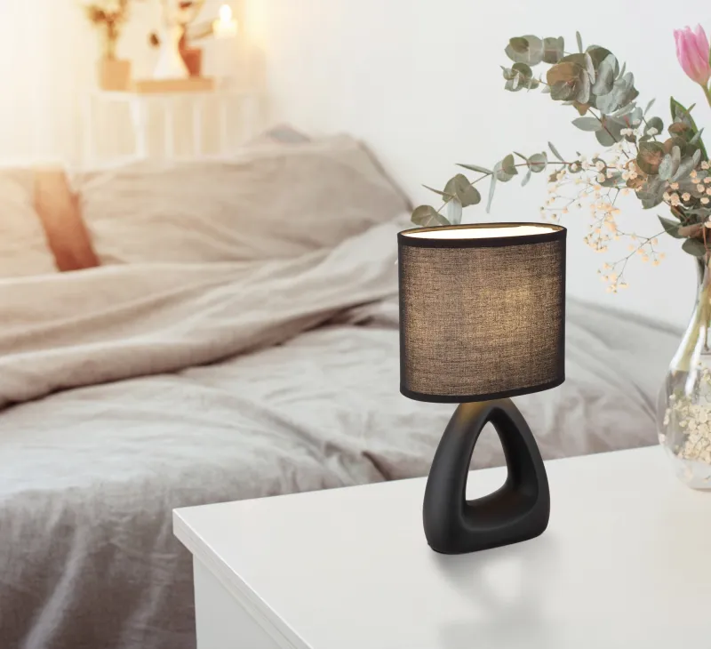 Triangle 30cm Svart bordlampe Fra Globo Lighting - Den triangelformade basen med ett stilrent utskuret h&aring;l ger ett modernt intryck, medan den ovala textilsk&auml;rmen i svart f&auml;rg sprider ett behagligt och j&auml;mnt ljus.