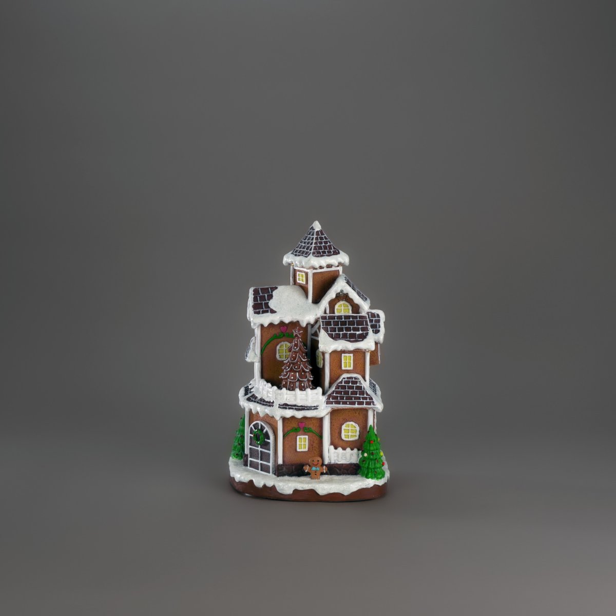 Pepperkakeby 30cm Brun Fra Konstsmide - Det detaljerte huset med sn&oslash;dekt tak, skinnende vinduer og dekorert grantre sprer en varm og innbydende gl&oslash;d i rommet.