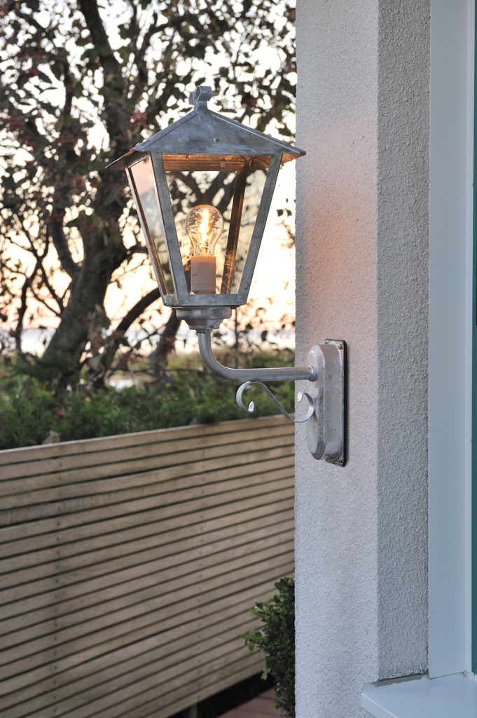 Benu Galvanisert stål utendørslampe Fra Konstsmide - Lampens klassiske lyktform og robuste materiale gj&oslash;r den til et perfekt valg for de som &oslash;nsker &aring; skape en innbydende atmosf&aelig;re ved innganger eller lange korridorer.