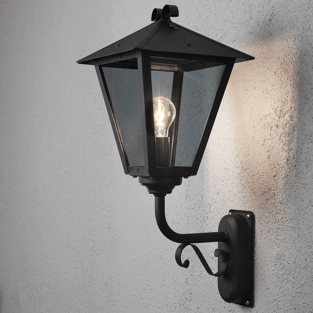 Benu Svart utendørslampe Fra Konstsmide - Lampens klassiske lyktform og robuste materiale gj&oslash;r den til et perfekt valg for de som &oslash;nsker &aring; skape en innbydende atmosf&aelig;re ved innganger eller lange korridorer.
