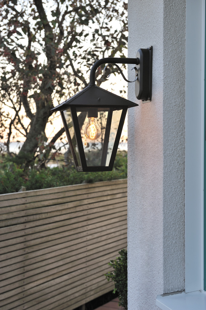 Benu Svart utendørslampe Fra Konstsmide - Lampens klassiske lyktform og robuste materiale gj&oslash;r den til et perfekt valg for de som &oslash;nsker &aring; skape en innbydende atmosf&aelig;re ved innganger eller lange korridorer.