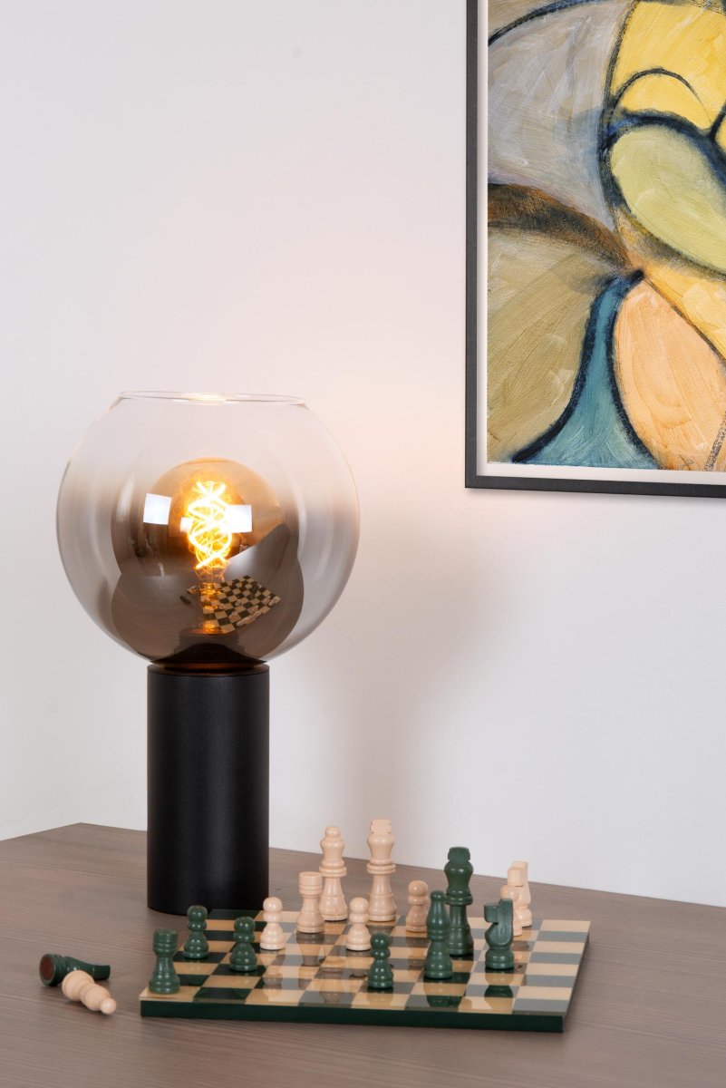 Marius 32cm Svart bordlampe Fra Lucide - Med en kompakt sylindrisk sokkel av metall og lampeskjerm i røkt glass klarer Marius seg like godt med; brystet, skrivebordet, salongbordet eller nattbordet.