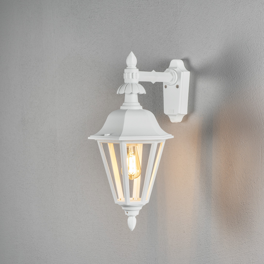 Pallas Hvit utendørslampe Fra Konstsmide - Med sitt lanterneformede design og klare glassfelt sprer lampen et varmt og innbydende lys som er perfekt for innganger, uteplasser og gangveier.