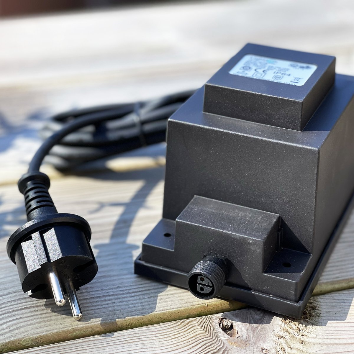 Transformator 105w Svart Fra Lightson - Transformatoren har en 12 volts hurtigkobling i den ene enden og en 2 meter lang ledning med støpsel i den andre, som du kobler til en vanlig stikkontakt.