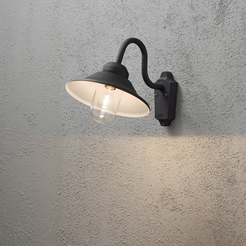 Vega Svart utendørslampe Fra Konstsmide - Med sin klassiske form og store skygge skaper den et behagelig og rettet lys, perfekt for entréer og uteplasser.