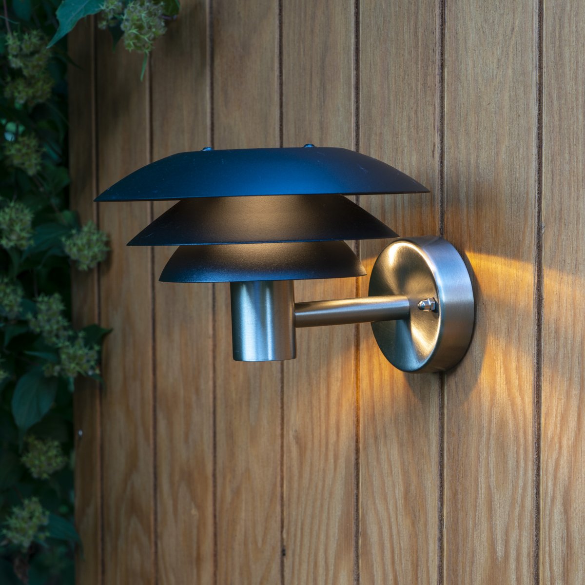 DL20 Rustfritt stål utendørslampe Fra Dyberg Larsen - Lampen har tre ikoniske skjermer i forskjellige størrelser som sprer et magisk lys og er laget av rustfritt stål med elegante matte sorte skjermer.
