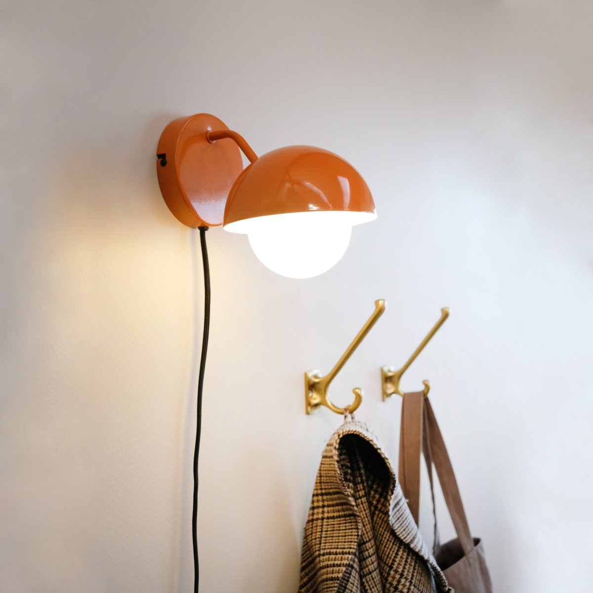 Rose Ø15 skinnende oransje vegglampe Fra Dyberg Larsen - Glasskuppelen fungerer som en naturlig lysspreder og skaper en varm og innbydende atmosfære i rommet.