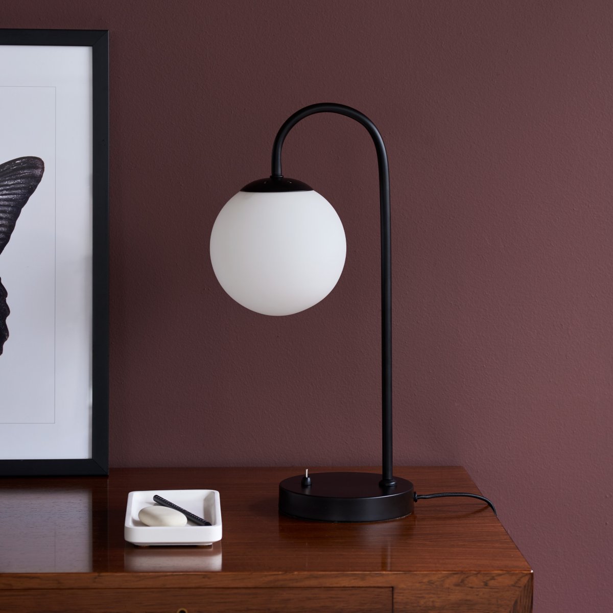Café Paris 46cm Svart bordlampe Fra Dyberg Larsen - Med en opalglassskjerm og metallbunn kombinerer den en moderne stil med en varm og innbydende følelse.