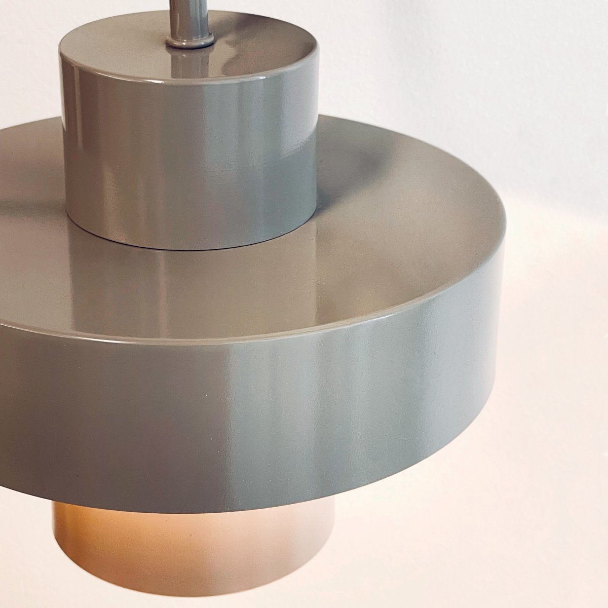 Stoke Ø15 Varm grå vegglampe Fra Dyberg Larsen - Den er laget av metall med en blank overflate som fremhever de sylindriske formene på lampen og skaper en balansert kontrast med andre materialer som stein, tre.