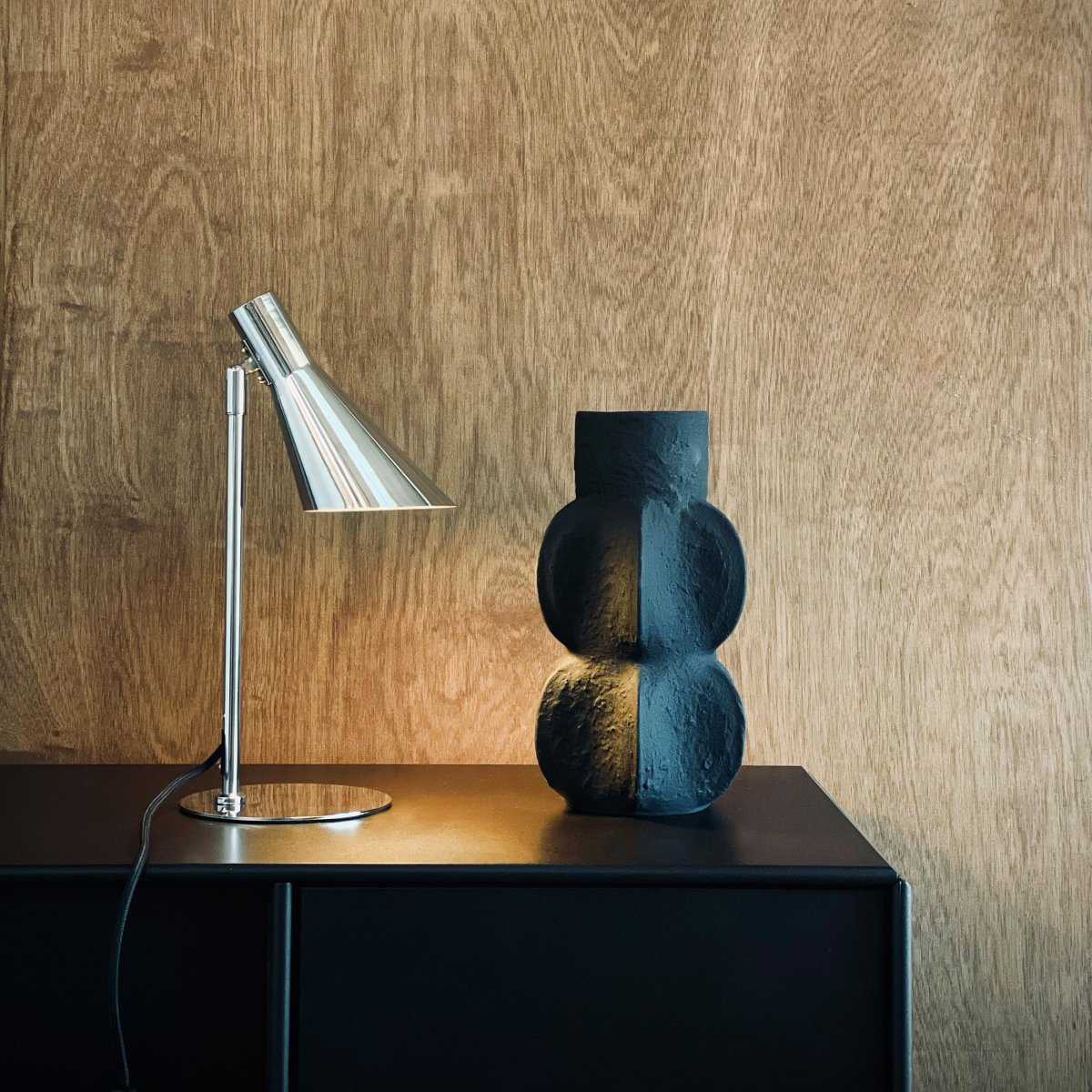 DL12 Mini 40cm Krom skrivebordslampe Fra Dyberg Larsen - Den er utstyrt med en skjerm som kan både roteres og vippes, noe som gjør det enkelt å rette lyset etter behov.