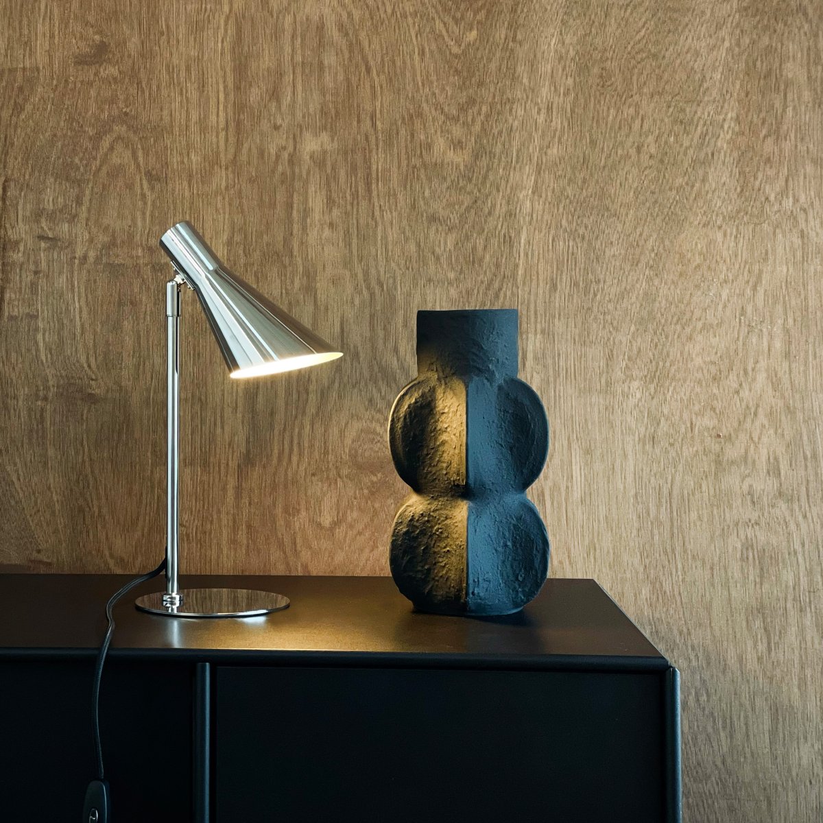 DL12 Mini 40cm Krom skrivebordslampe Fra Dyberg Larsen - Den er utstyrt med en skjerm som kan både roteres og vippes, noe som gjør det enkelt å rette lyset etter behov.