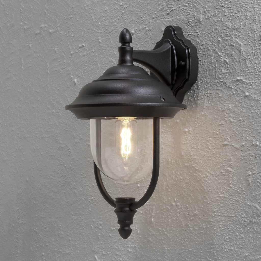 Parma Svart utendørslampe Fra Konstsmide - Med sin vakre form og klare glasskuppel sprer den et varmt og innbydende lys, ideelt for innganger og uteplasser.