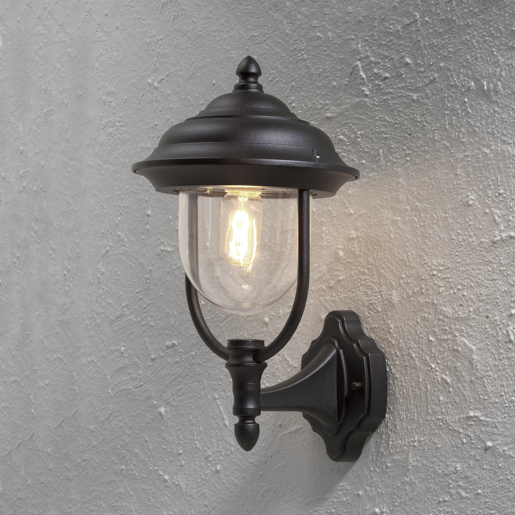 Parma Svart utendørslampe Fra Konstsmide - Med sin vakre form og klare glasskuppel sprer den et varmt og innbydende lys, ideelt for innganger og uteplasser.