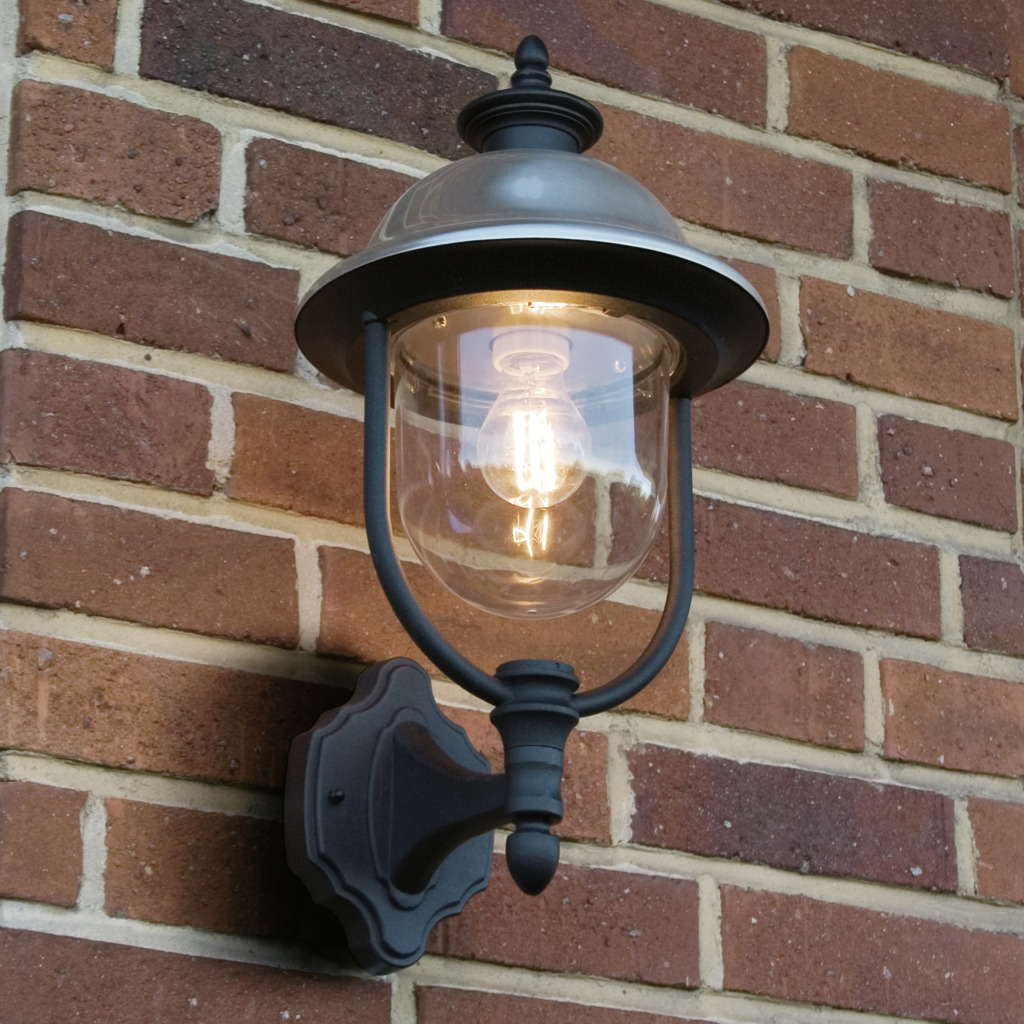 Parma Svart utendørslampe Fra Konstsmide - Med sin robuste svarte finish og klare glasskuppel sprer den en varm og innbydende glød, og skaper en innbydende atmosfære ved inngangen eller uteplassen.