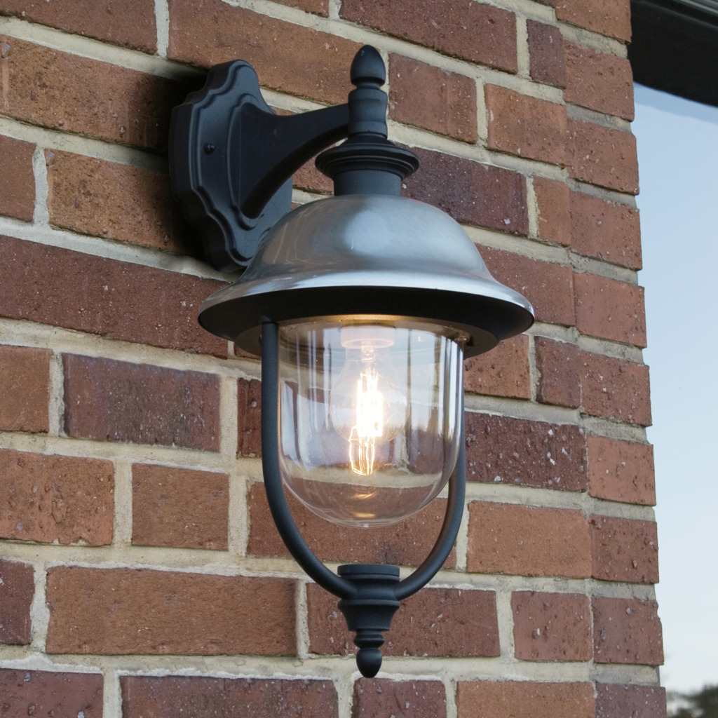 Parma Svart utendørslampe Fra Konstsmide - Med sin robuste svarte finish og klare glasskuppel sprer den en varm og innbydende glød, og skaper en innbydende atmosfære ved inngangen eller uteplassen.