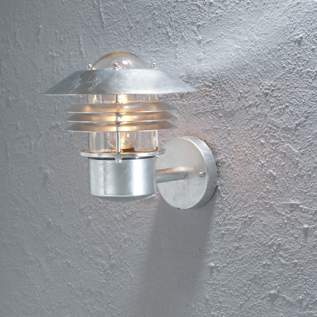 Modena Galvanisert stål utendørslampe Fra Konstsmide - Med sitt beskyttende tak og stilige design gir den et behagelig og rettet lys, ideelt for å skape en trygg og innbydende atmosfære utendørs.