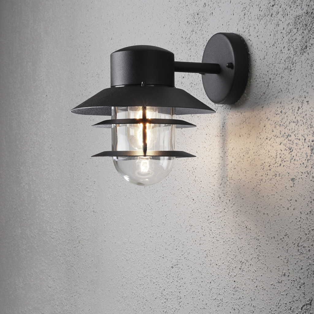 Modena Svart utendørslampe Fra Konstsmide - Med sitt beskyttende tak og stilige design gir den et behagelig og rettet lys, ideelt for å skape en trygg og innbydende atmosfære utendørs.