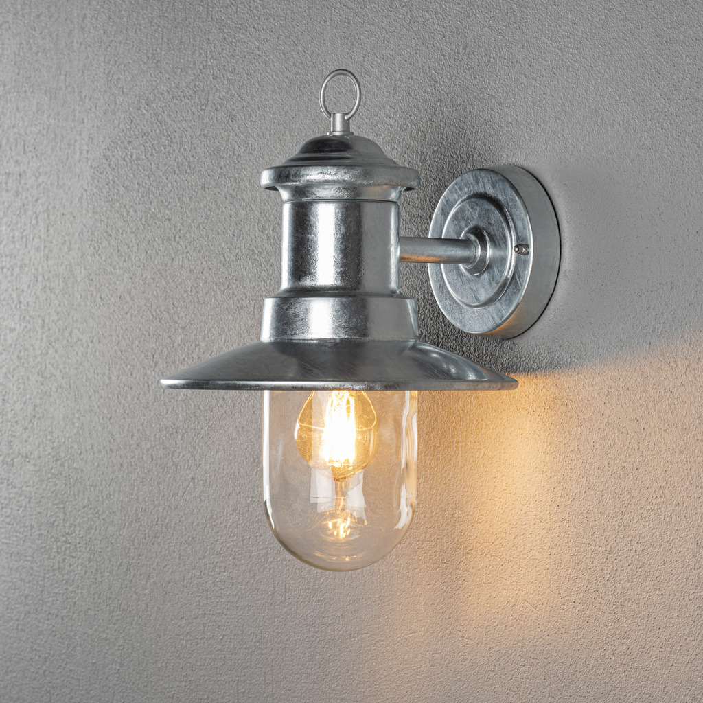 Napoli Varmgalvanisert utendørslampe Fra Konstsmide - Lampens klassiske design med rund glasskuppel og bred skjerm sprer et varmt og behagelig lys, perfekt for å lyse opp innganger og uteplasser.