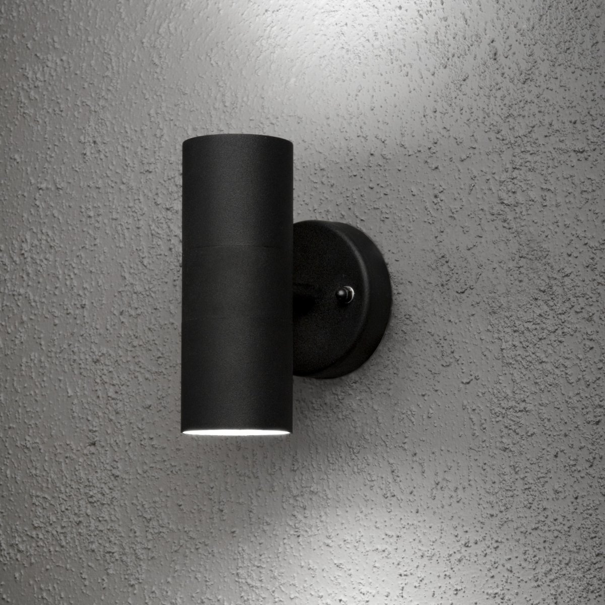 Modena Svart utendørslampe Fra Konstsmide - Lampen sprer lyset b&aring;de oppover og nedover og skaper et dekorativt lysbilde som fremhever fasaden og gir en innbydende f&oslash;lelse utend&oslash;rs.
