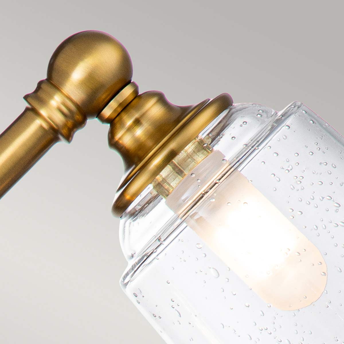 Huguenot Lake 53cm Messing baderomslampe Fra Elstead Lighting - De elegante sirkulære detaljene og håndkuttede brakettene gir en følelse av tradisjonelt håndverk, mens det klare, strukturerte glasset skaper et mykt og innbydende lys.
