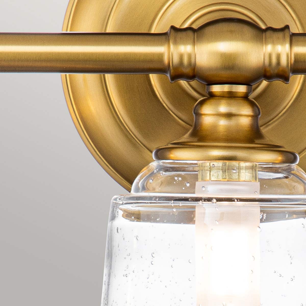 Huguenot Lake 53cm Messing baderomslampe Fra Elstead Lighting - De elegante sirkulære detaljene og håndkuttede brakettene gir en følelse av tradisjonelt håndverk, mens det klare, strukturerte glasset skaper et mykt og innbydende lys.