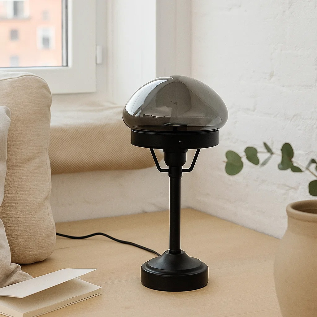 Jas 30cm Svart bordlampe Fra Lampan - Den har en svart metallbase og en kuppelformet lampeskjerm i r&oslash;kt glass som sprer et mykt og behagelig lys.