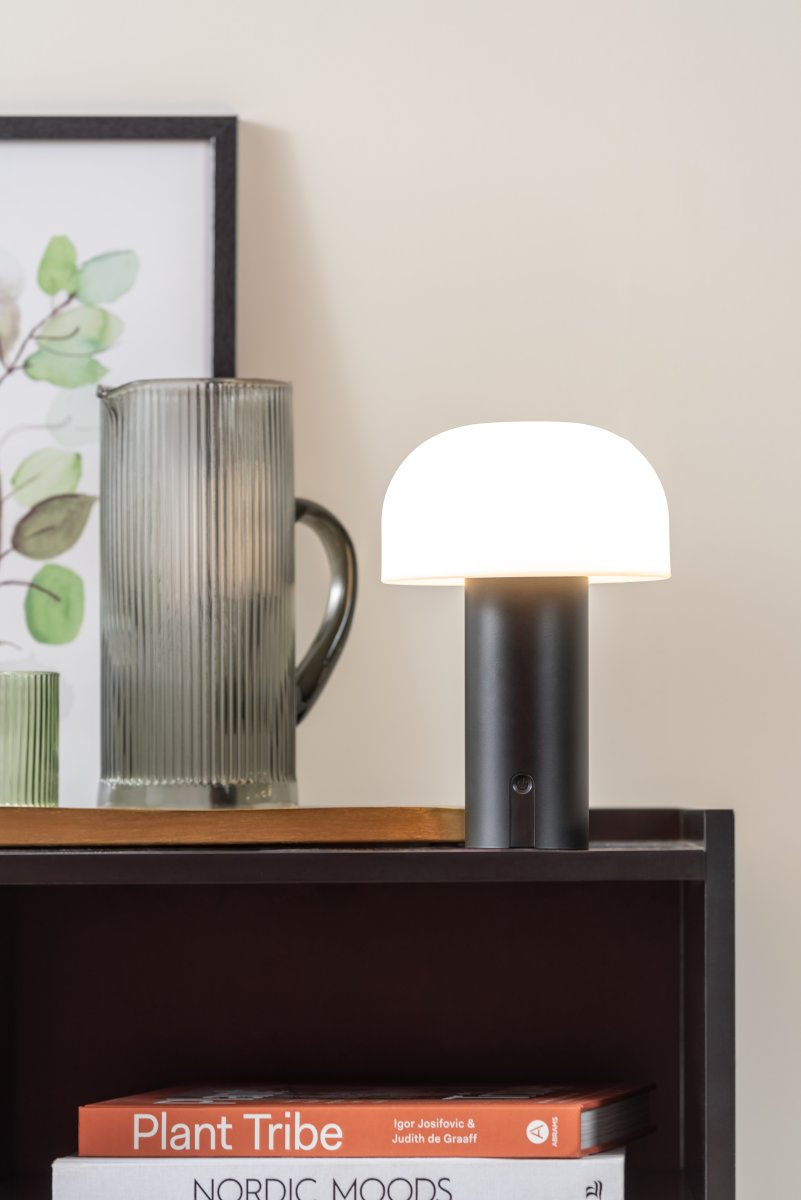 Luca LED 22cm Svart bærbar Fra Leitmotiv - Den er laget av metall med en matt svart finish og har en melkehvit plastskjerm som sprer et mykt og behagelig lys.