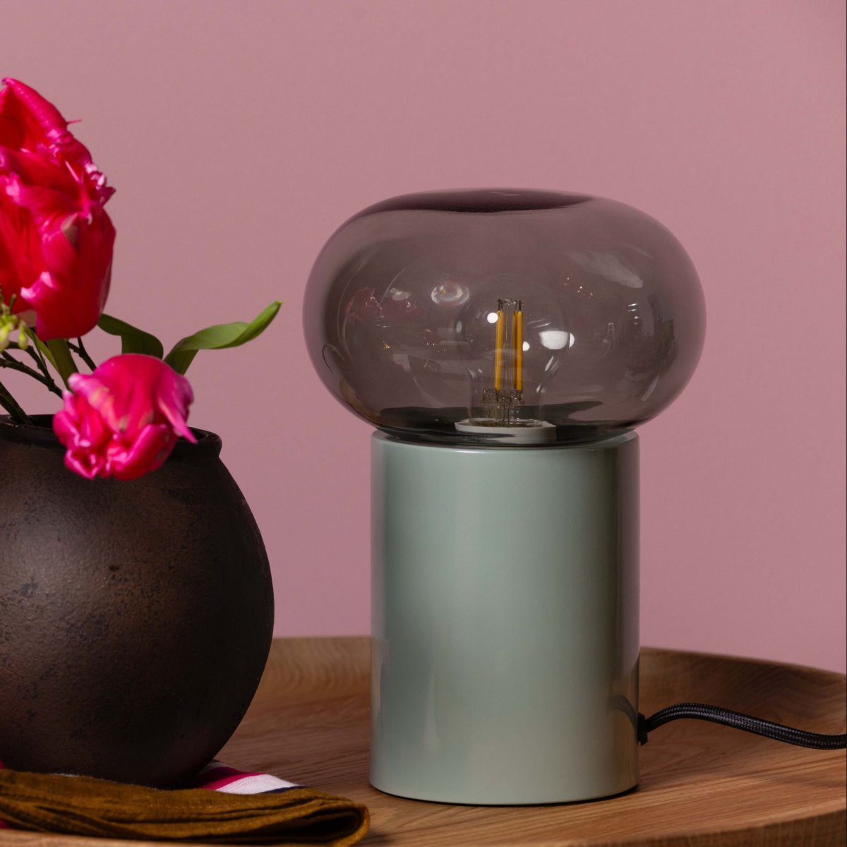 Knut 22cm Grønn bordlampe Fra Brilliant - Den gr&oslash;nne lampebasen gir et friskt og livlig uttrykk, mens den r&oslash;ykfargede glassskjermen skaper en myk og stemningsfull lysfordeling.
