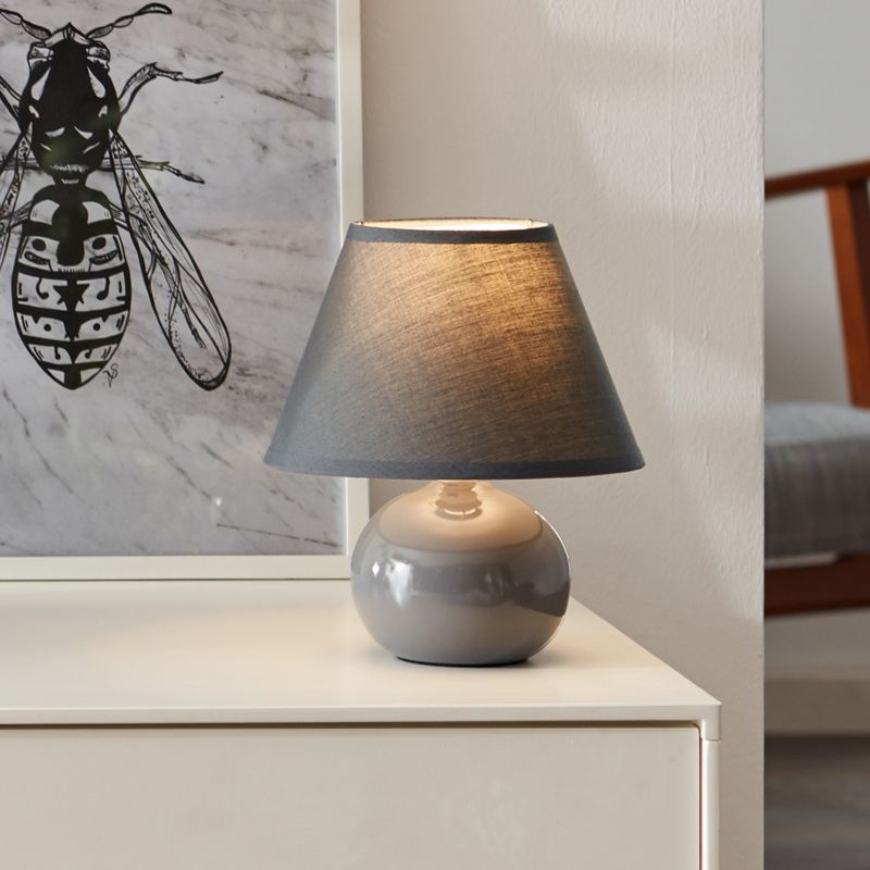 Primo 23cm Mørkegrå bordlampe Fra Brilliant - Den er laget av tekstil og keramikk og gir et behagelig lys.